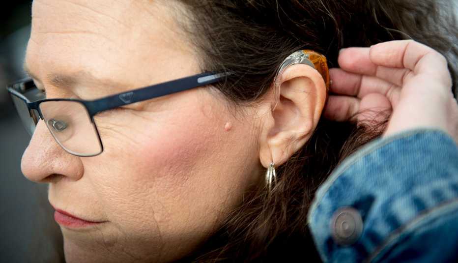 A woman moves her hair away from her ear showing her hearing aid