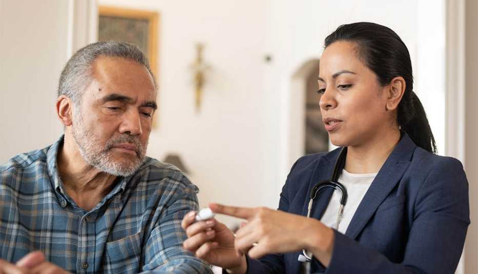 A Hispanic female doctor is talking to her senior male patient during a home medical visit. She is showing him how to use a diabetes kit.