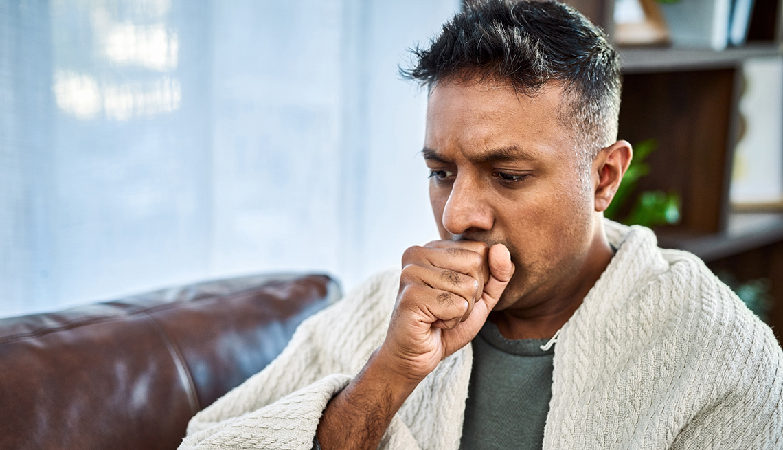 a man coughing while recovering from an illness on the sofa at home