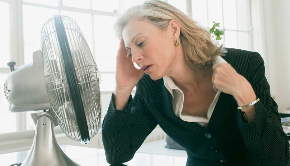 Mature woman in a business suit sitting in front of electric fan, looking uncomfortably hot.