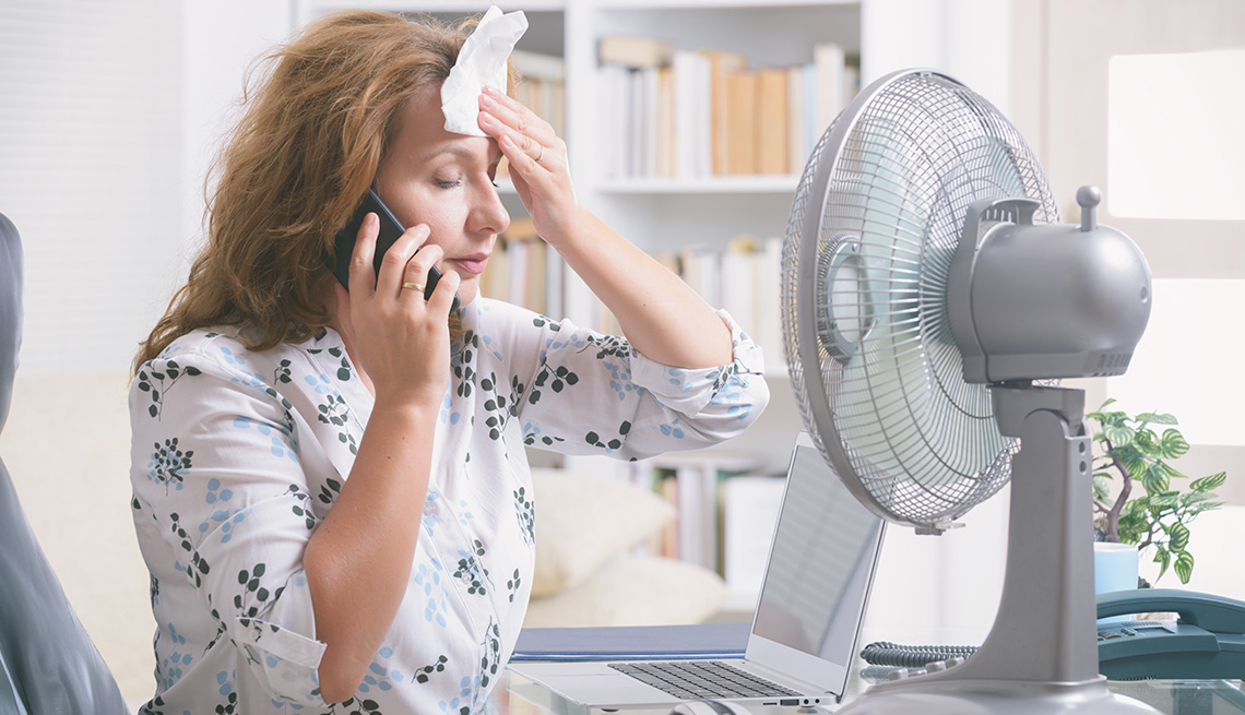 menopausal woman sitting in front of a fan and blotting her head during a severe hot flash