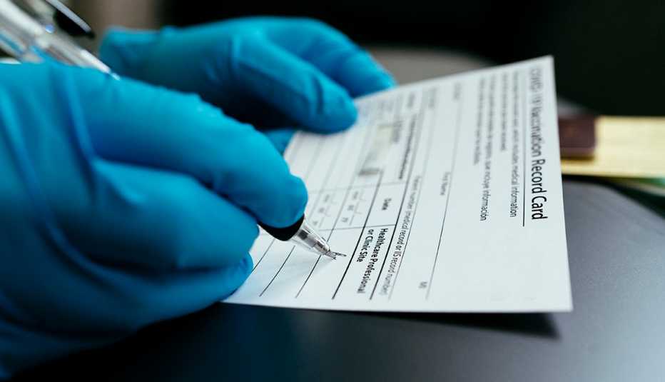 close up of doctor's hand filling out a vaccine card while wearing medical gloves