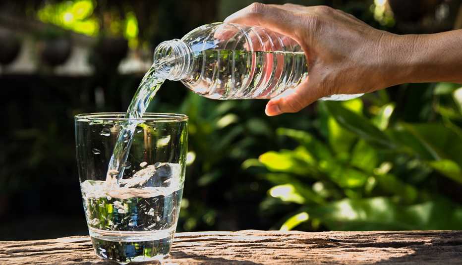 close up of a woman pouring water from a plastic bottle into a glass on an outdoor background to reflect the dangers of drinking too much water also known as hyponatremia