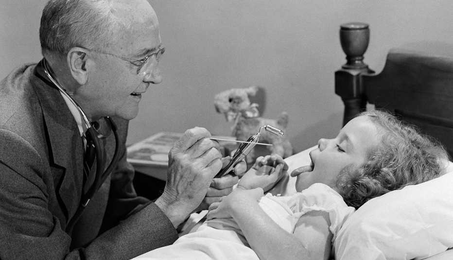 a black and white photo of a doctor making a house call to examine a sick child in bed