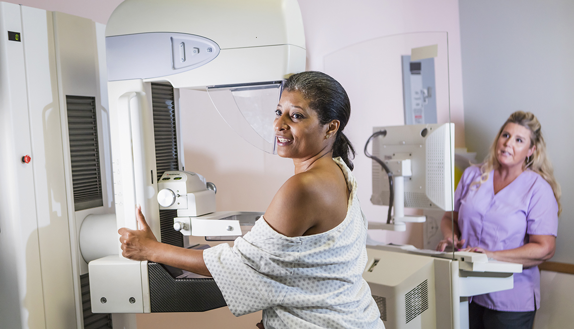 woman wearing a hospital gown, getting her annual mammogram, technologist in background
