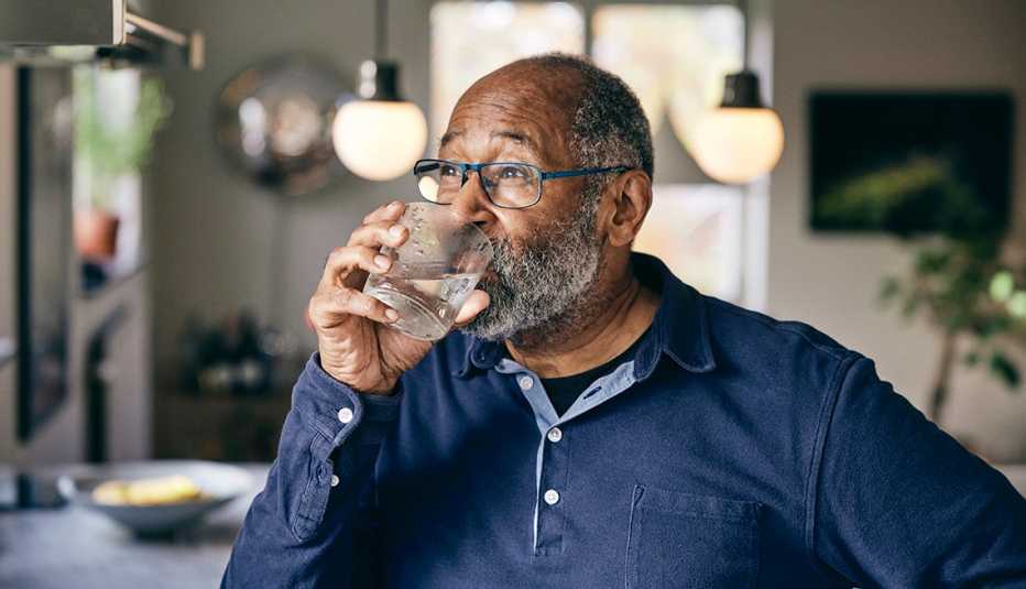 a man in a long sleeve blue shirt drinks water in his kitchen on a hot summer day