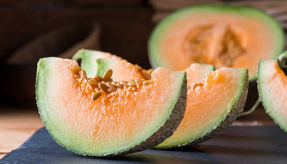 close up of slices of cantaloupe on a table with a large halved cantaloupe in the background recalled due to the cantaloupe salmonella outbreak 2023