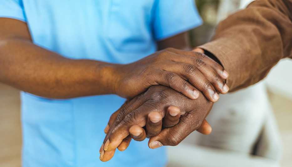 Home caregiver and senior man holding hands.