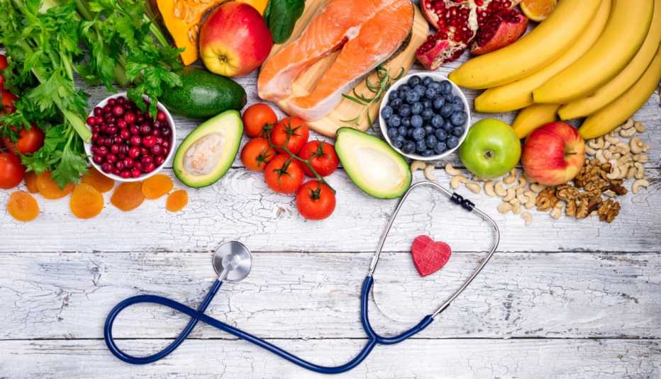 stethoscope framing a red paper heart and a grouping of salmon, avocados, apples and other heart-healthy foods
