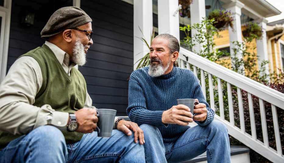 two friends sitting on the front steps of a porch talking and drinking coffee