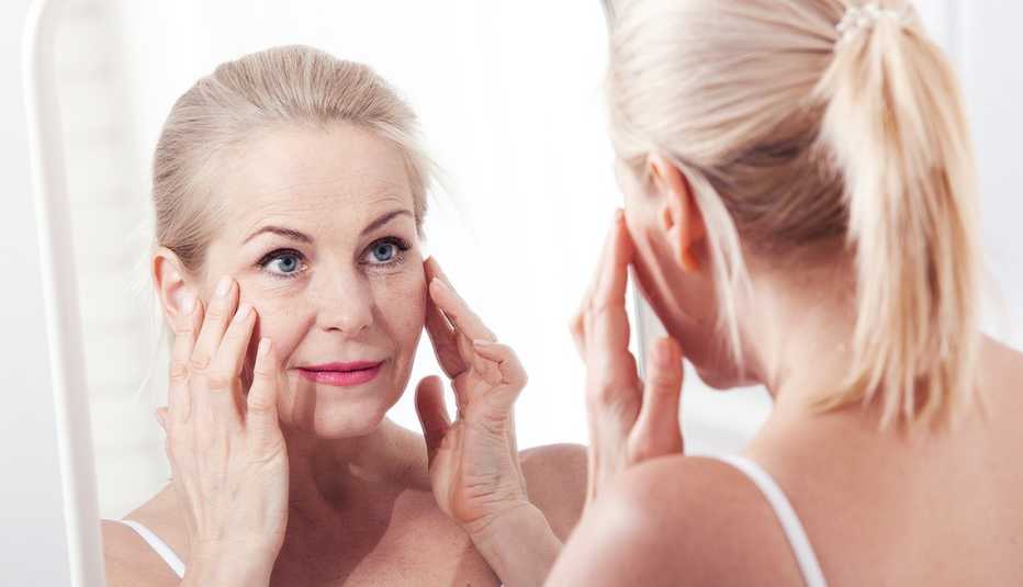 Woman inspects the skin around her eye in the mirror