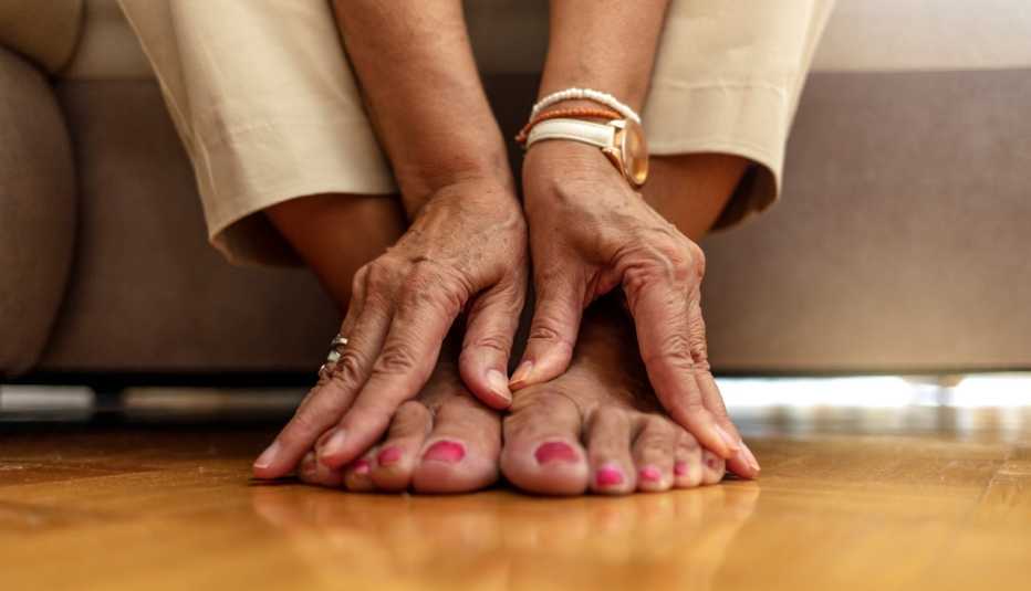 close up of a woman's hands massaging her feet and toes on a hardwood floor