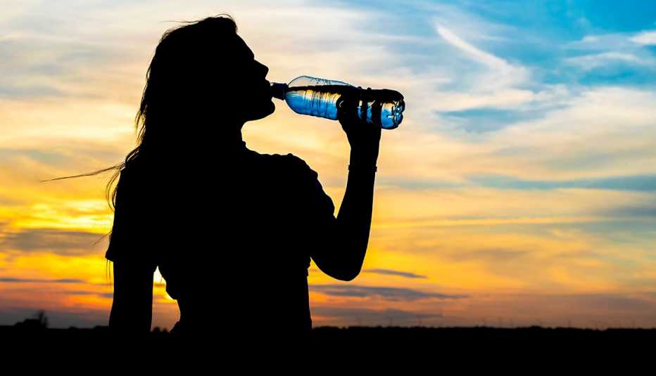 silhouette of a woman drinking from a water bottle filled with nanoplastics on the background of a summer sunset