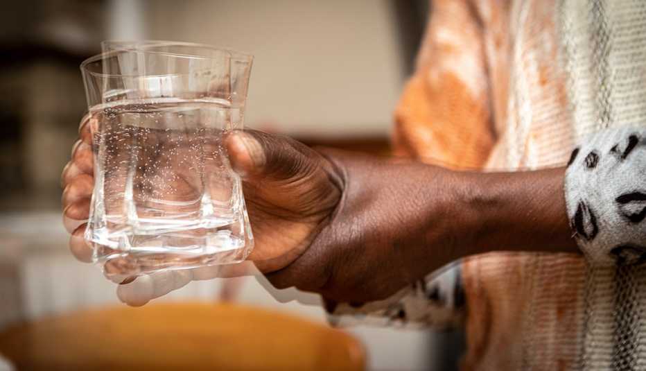 Close shot of a person with a hand tremor holding a glass of water and the glass is shaking