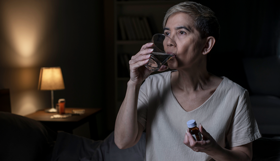a woman taking melatonin capsules with a glass of water in her bedroom at night