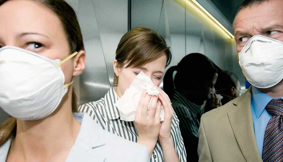 people wearing flu masks in an elevator with a sneezing woman