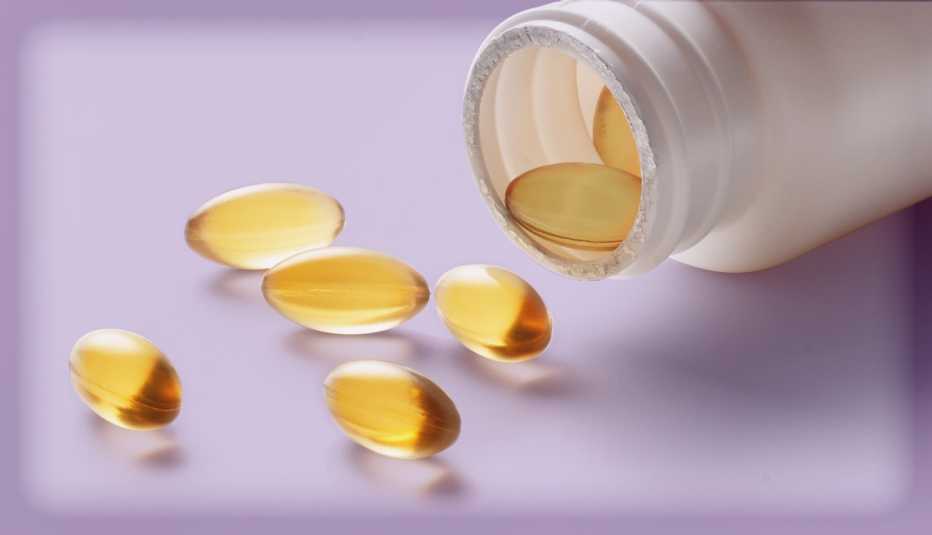 A bottle of C B D pills lies on its side with five translucent gold-colored pills outside of the bottle opening