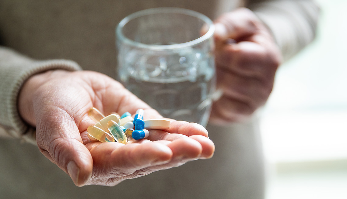 A person is holding several pill capsules in their hand along with a glass of water