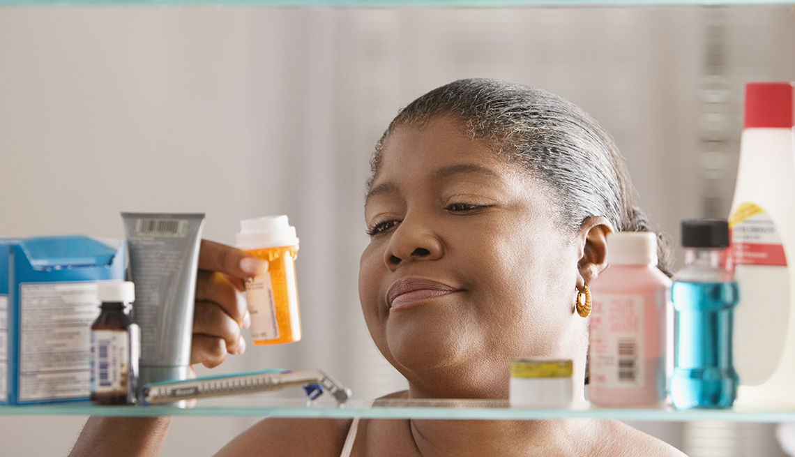 African American woman holding bottle of pills in front of medicine cabinet