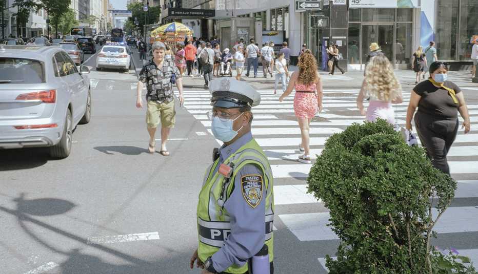 new york city street scene with policeman directing traffic and pedestrians crossing the street at a crosswlk