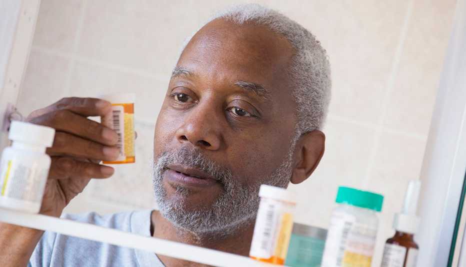 Man looks at prescription bottle at medicine cabinet