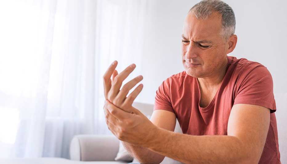 Mature man suffering from wrist pain at home while sitting on sofa during the day. Clenched painful hands
