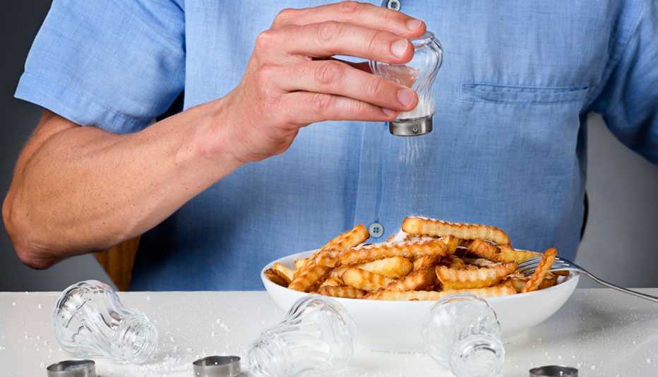 A person is pouring salt onto french fries