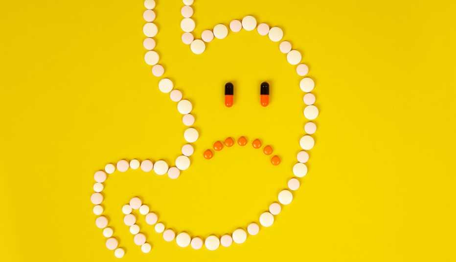 A stomach outline of pills with a sad face on a yellow background symbolizing stomach and digestive problems.