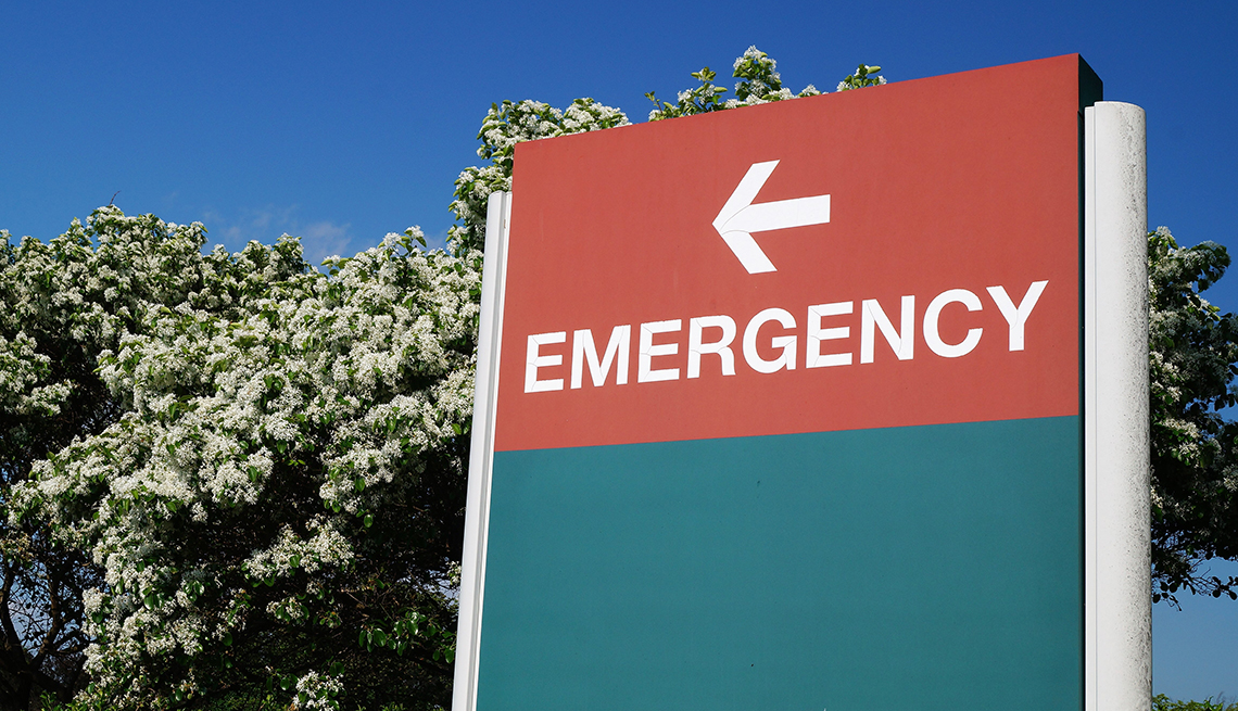 An outdoor green and red sign pointing in the direction of the hospital emergency department.