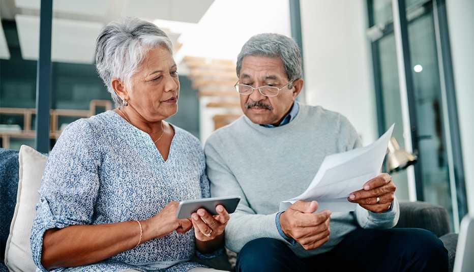 Shot of a mature couple using a cellphone while going through paperwork together at home