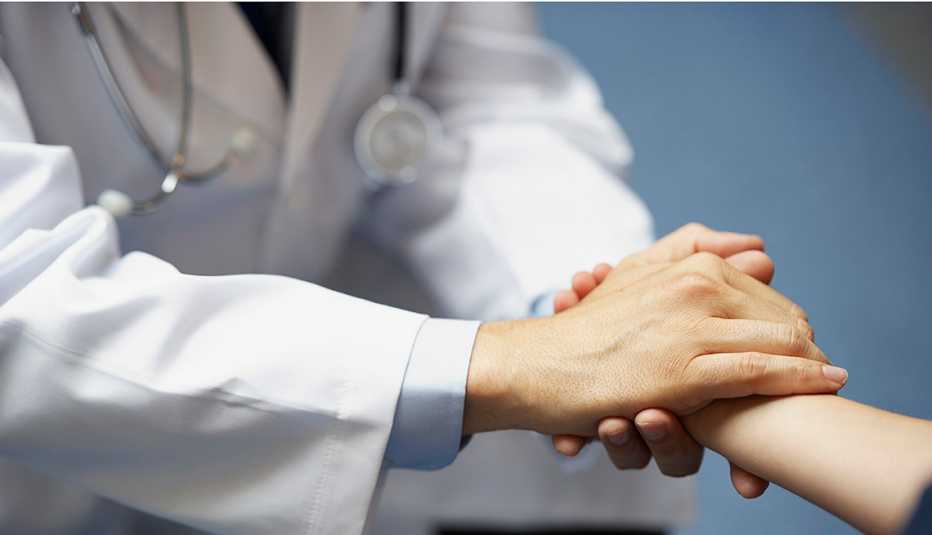 The torso of a doctor in a white lab coat with stethoscope holding a patient's hand.
