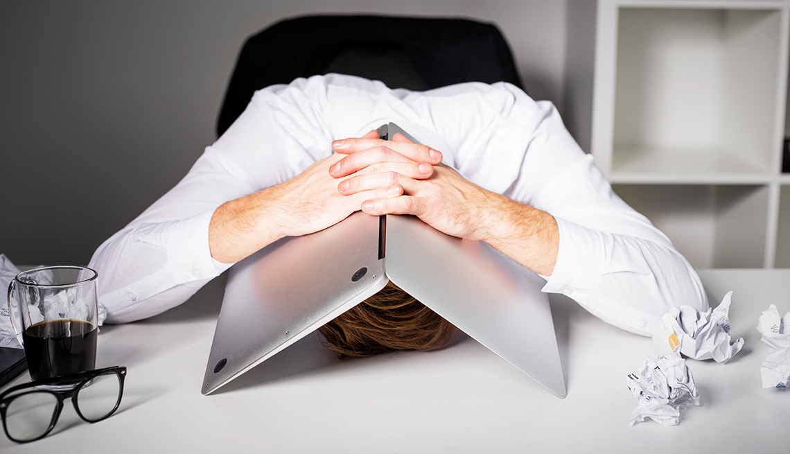 A man hides his head underneath his laptop