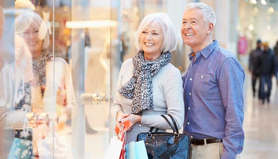 A happy couple looking at a store display while carrying shopping bags in a mall