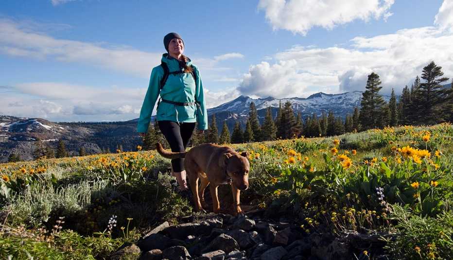 A woman hikes with her dog through a field of wildflowers in Desolation Wilderness with the Crystal Range in the background near South Lake Tahoe, California