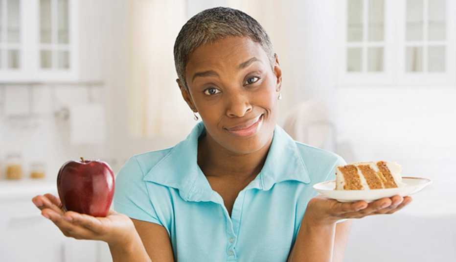 Mature African American woman deciding between eating an apple and a piece of cake.