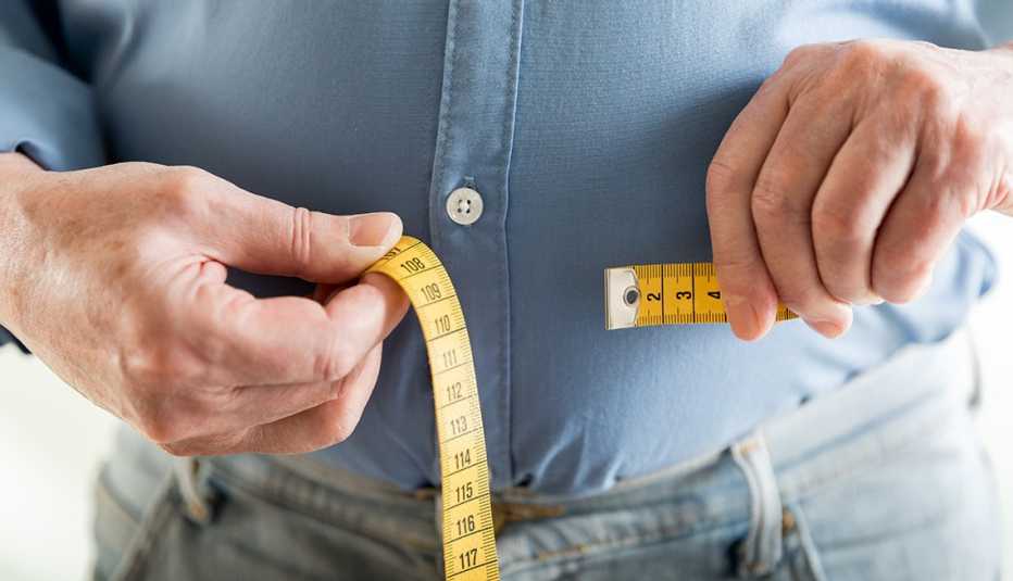 A man uses a tape measure to measure his stomach