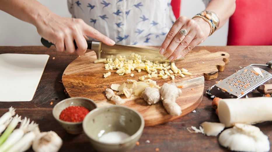 woman chopping ginger on a cutting board with garlic and other ingredients around it
