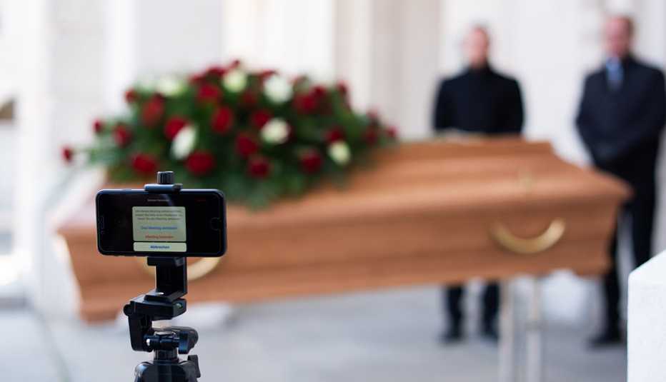 Two men standing near a casket. A video camera is in the foreground ready to  live stream the services