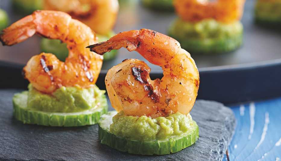 appetizers of grilled shrimp atop a cucumber slice and guacamole