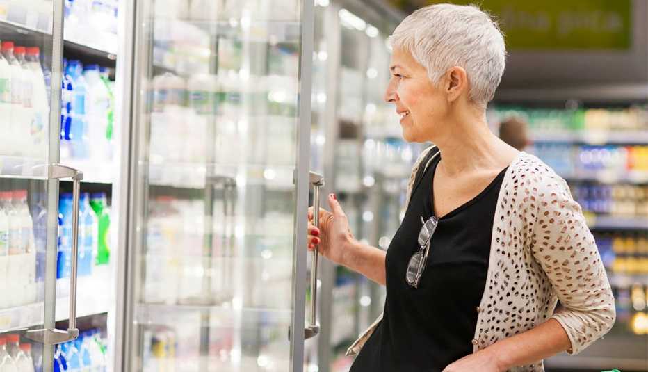 Mature woman shopping at supermarket opening fridge