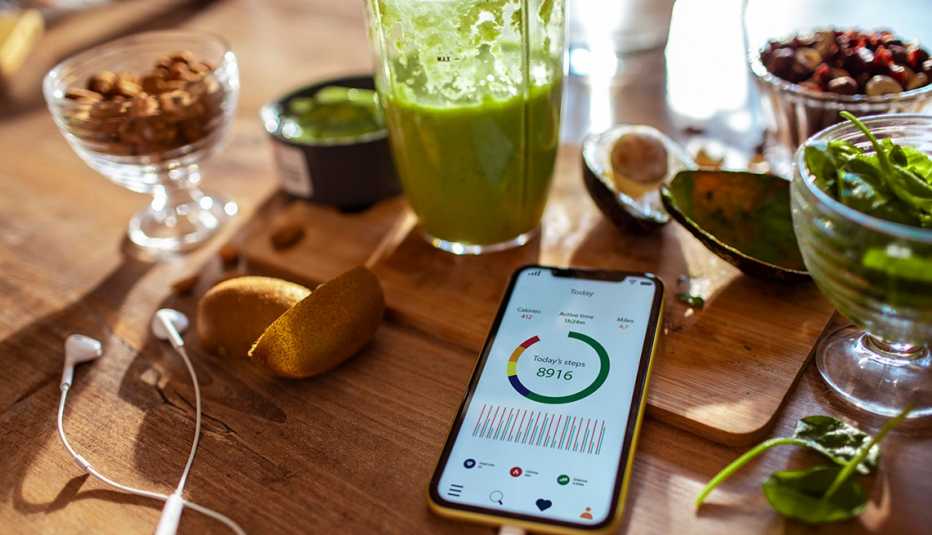A phone with a step-tracking health app, a juice cleanse drink and healthy food in the background