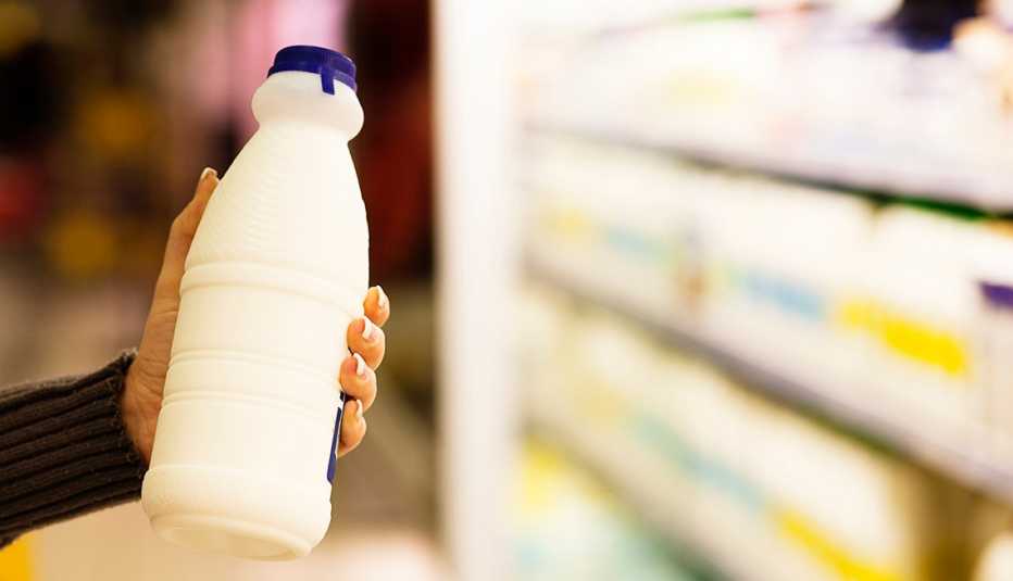 Woman's hand takes a bottle of milk from refrigerated shelves at a supermarket. 