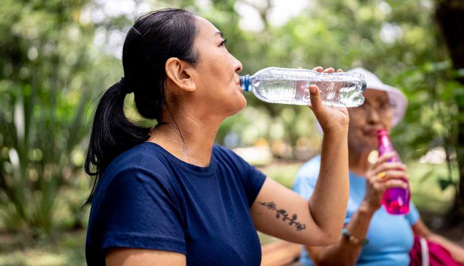 a dark haired woman drinks a bottle of water in a park