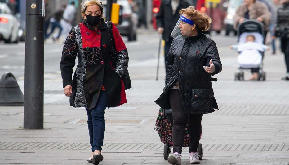Two women wearing a protective face mask and a plastic face shield on a London street.