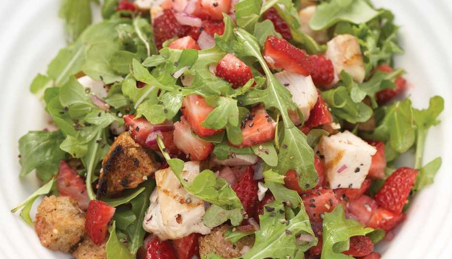 close up of a plate full of arugula salad with strawberries and chicken