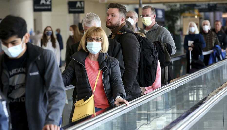 Air travelers, some with face masks and others without, use the moving walkway toward their gate at Midway International Airport in Chicago, Tuesday April 19, 2022. (
