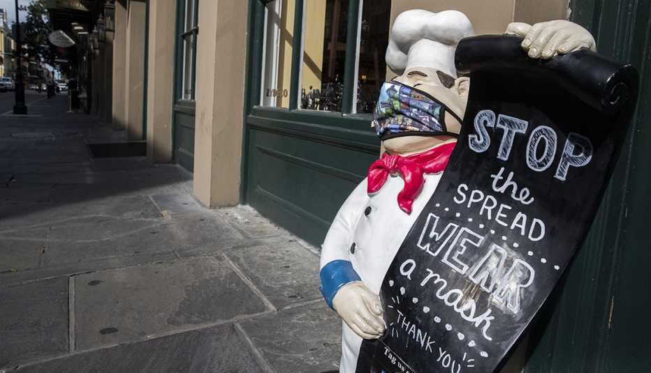 Statue of chef in New Orleans wearing a face mask holding a sign that says "stop the spread-wear a mask"