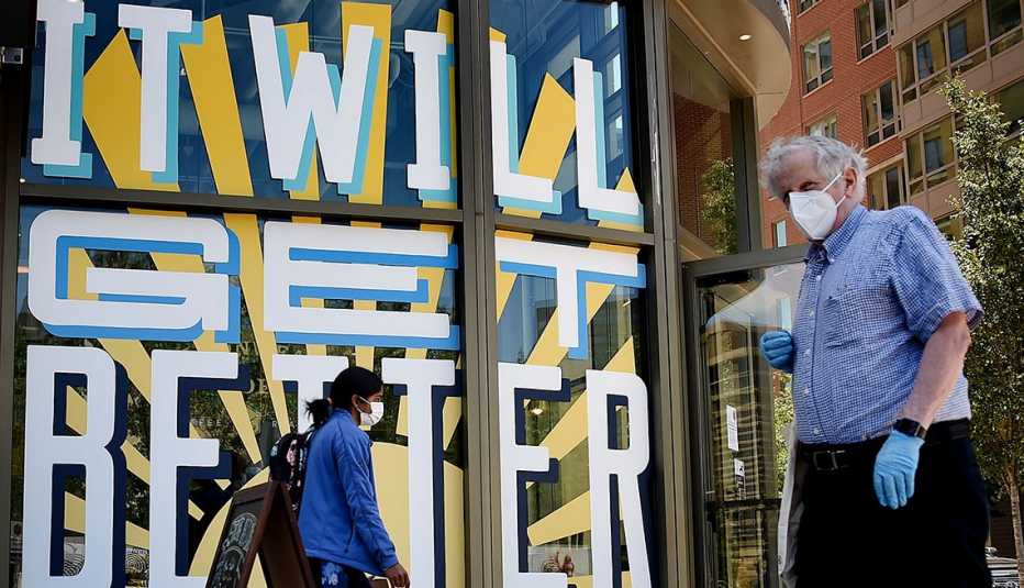 Man and woman in Arlington, Virginia walk past a mural that says It Will Get Better while wearing a mask.