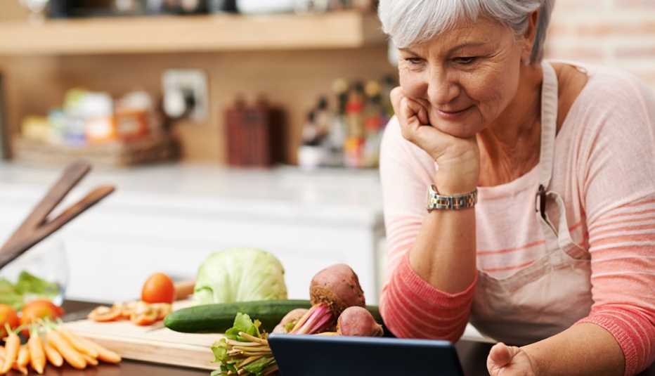 woman in kitchen looks at tablet, vegetables on counter to her right