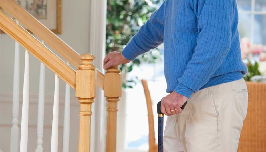Man in a blue sweater stands in front of stairs while holding a cane